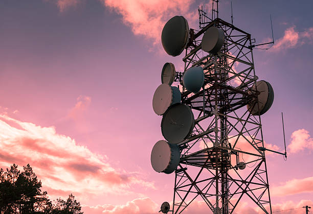 Remote telecommunications tower in a rural landscape with microwave dish alignment being corrected by a field technician